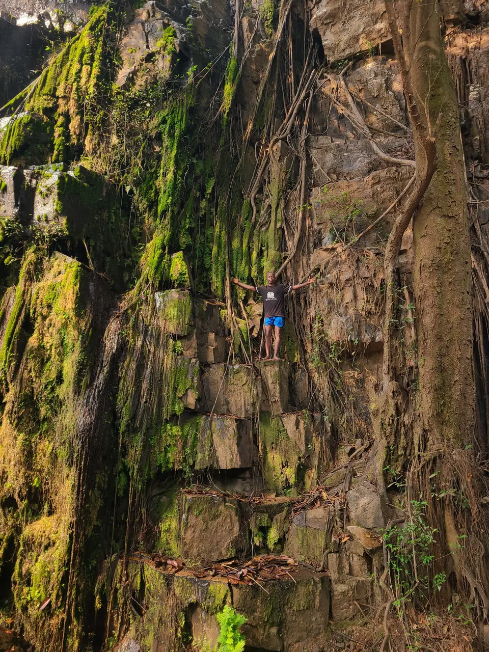 Visitor beside the tall rock walls and falling water at Karera Waterfalls in Burundi